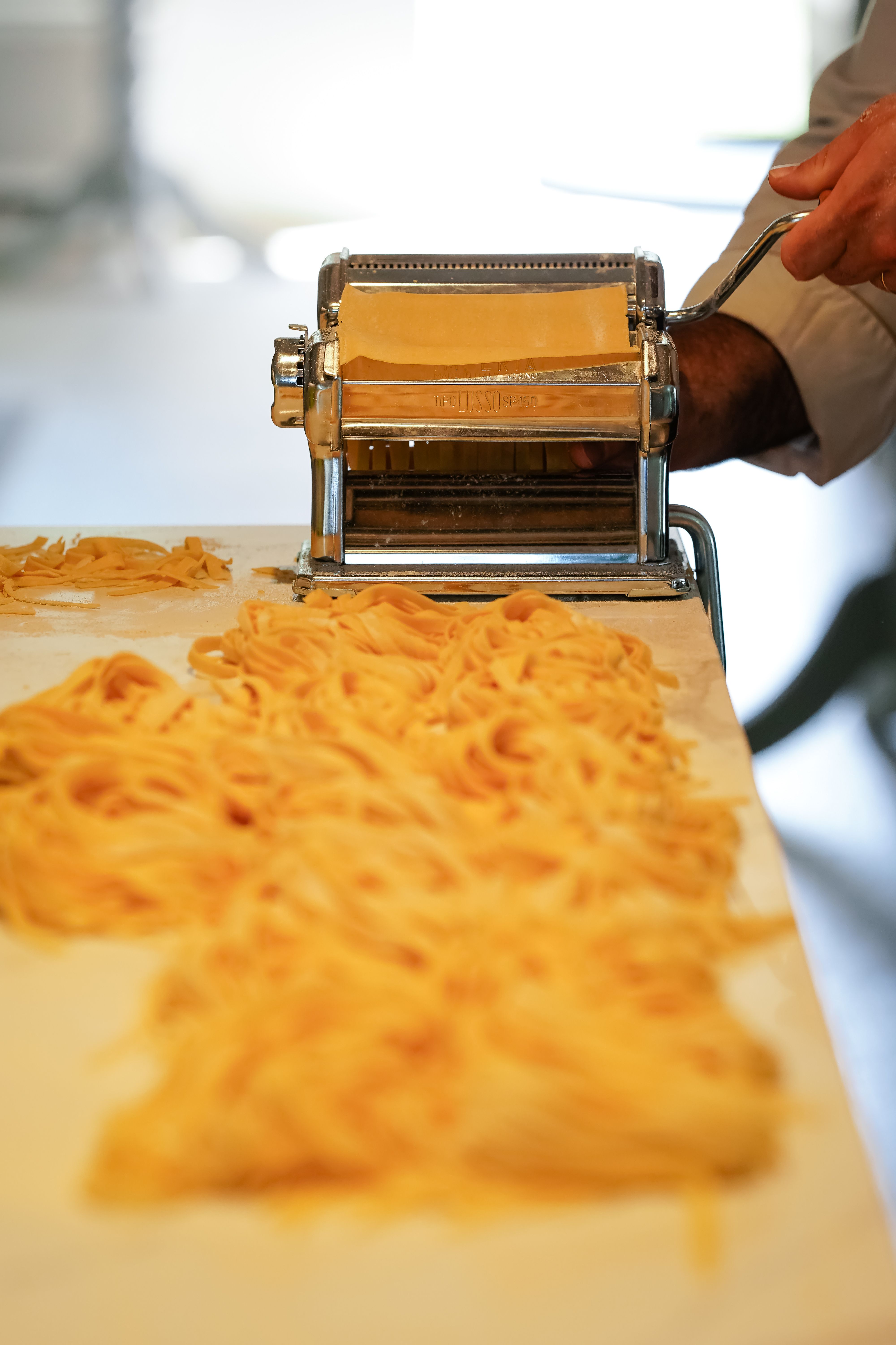 Fresh pasta being rolled through a pasta machine